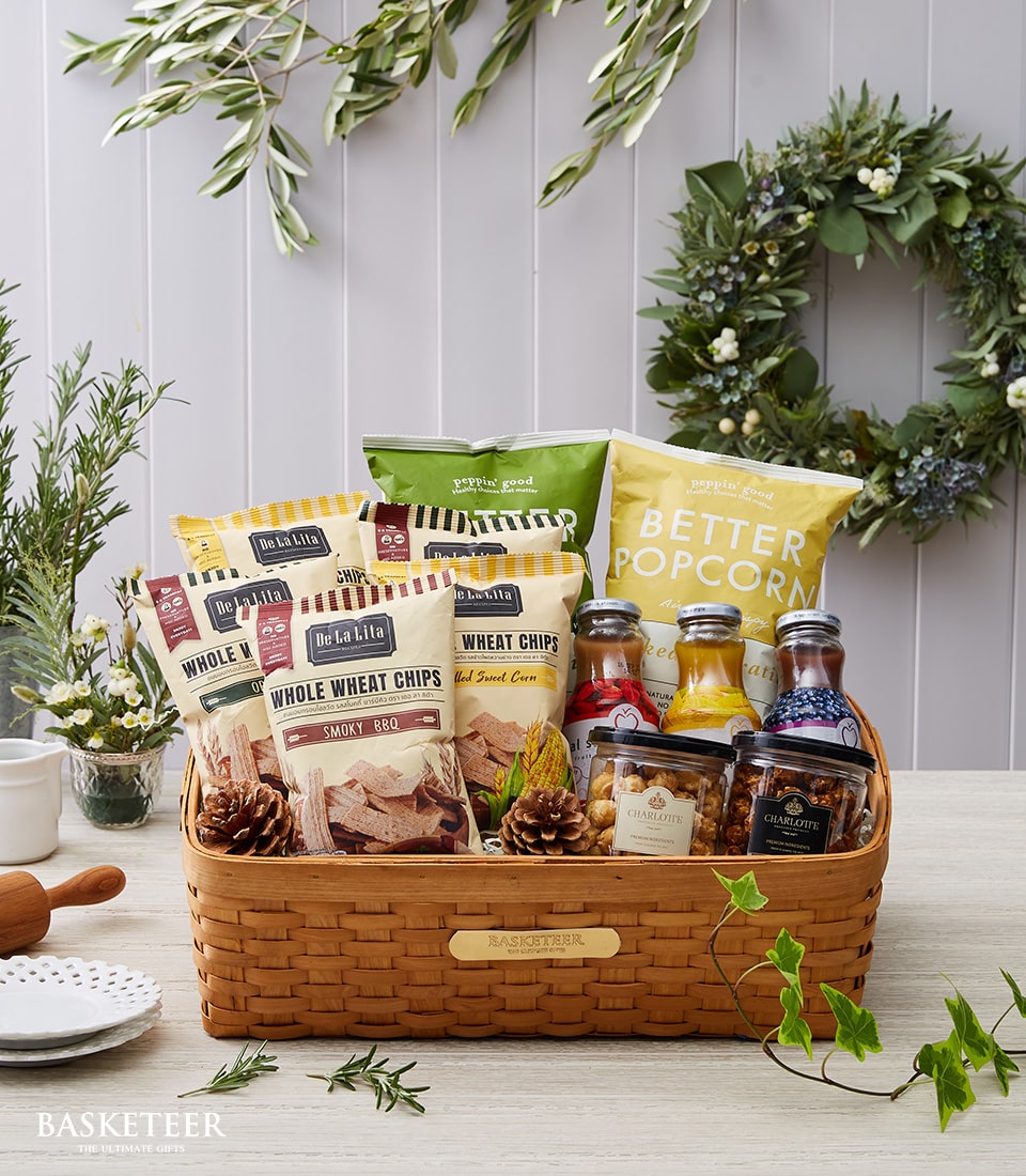 Woven gift basket filled with whole wheat chips, popcorn, artisan beverages, and gourmet preserves for health-conscious