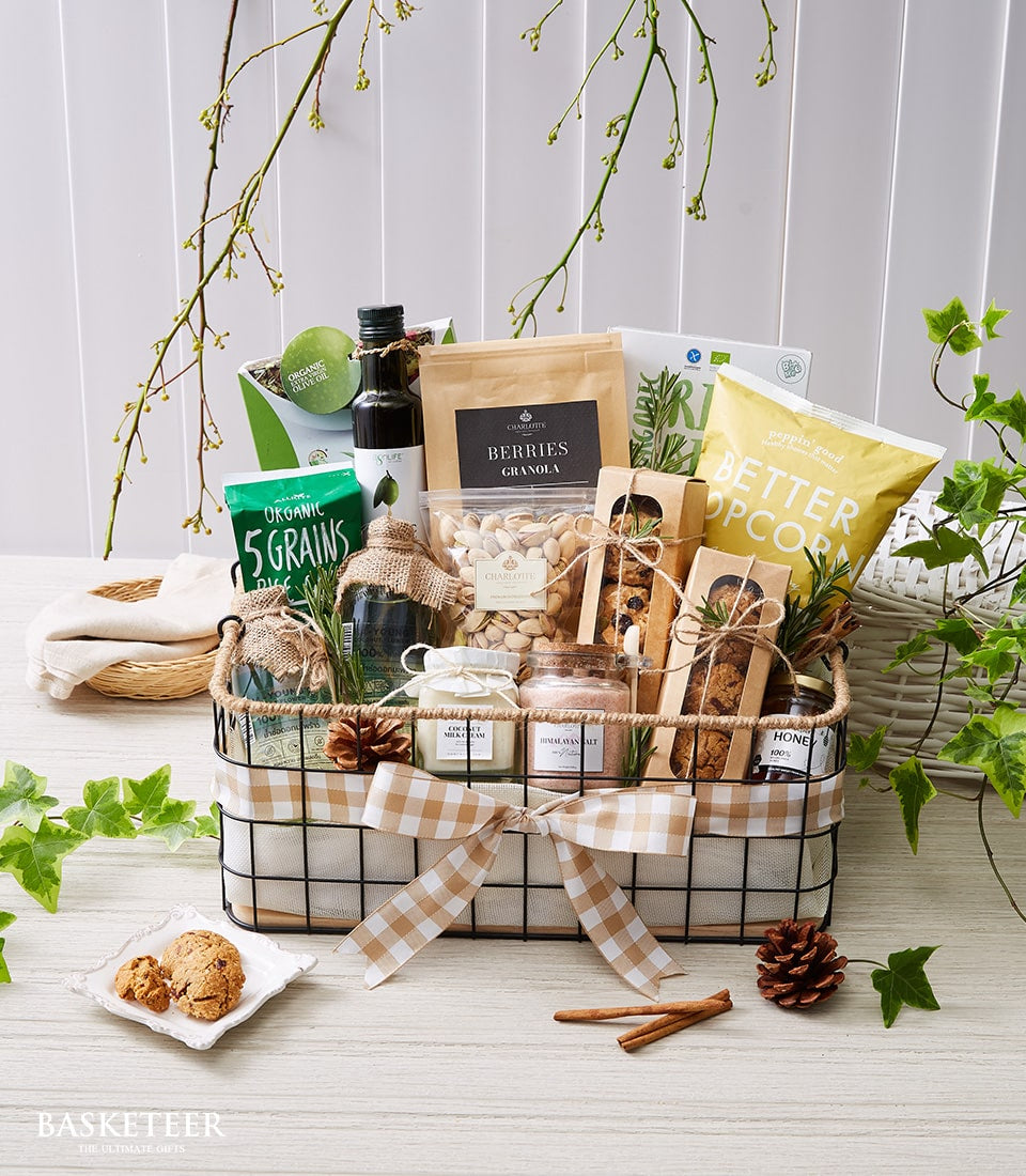 Black wire basket with gourmet organic foods, grains, granola, nuts, and artisan baked goods, tied with gingham ribbon