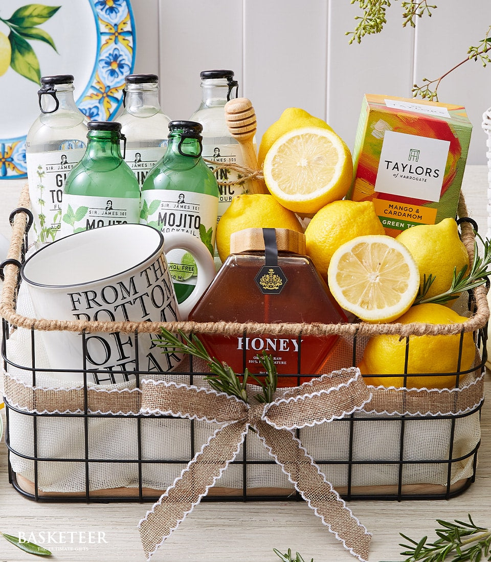 Black wire gift basket with fresh lemons, tea, honey, and ceramic mug for refreshing homemade beverages