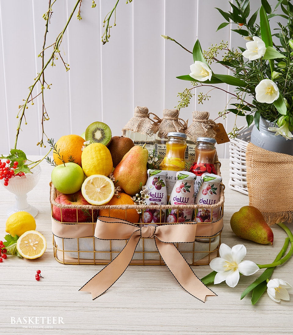 Gold wire basket with fresh citrus, apples, kiwi, pears, wellness juices and yogurts, light beige ribbon bow