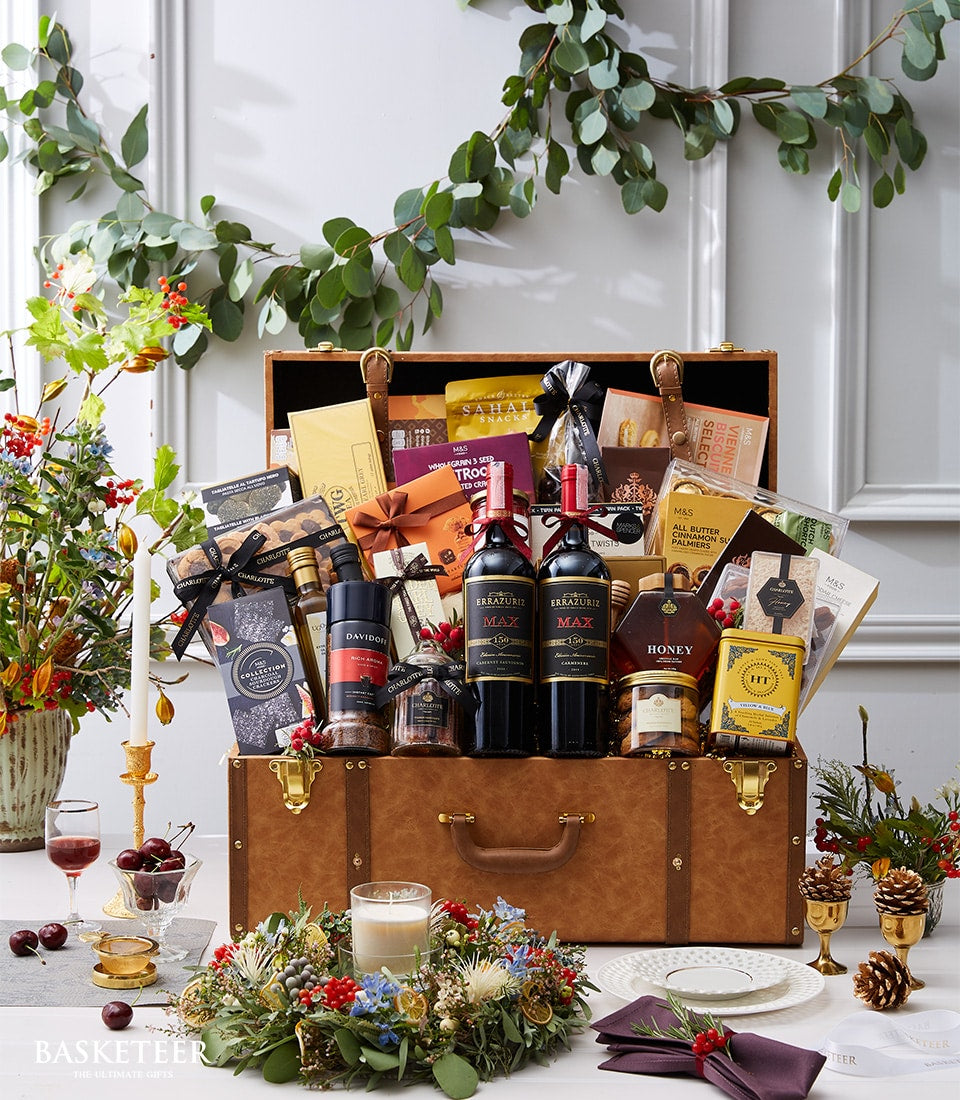 Luxury wine and gourmet hamper in brown leather trunk with red wine, artisan biscuits, honey, and preserves