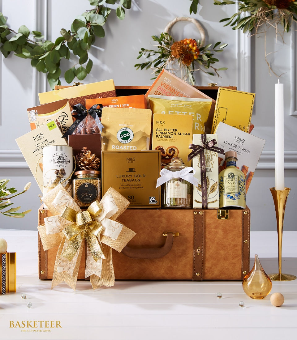 Luxury leather trunk gift hamper overflowing with gourmet chocolates, tea, coffee, and artisan treats with gold ribbon bow