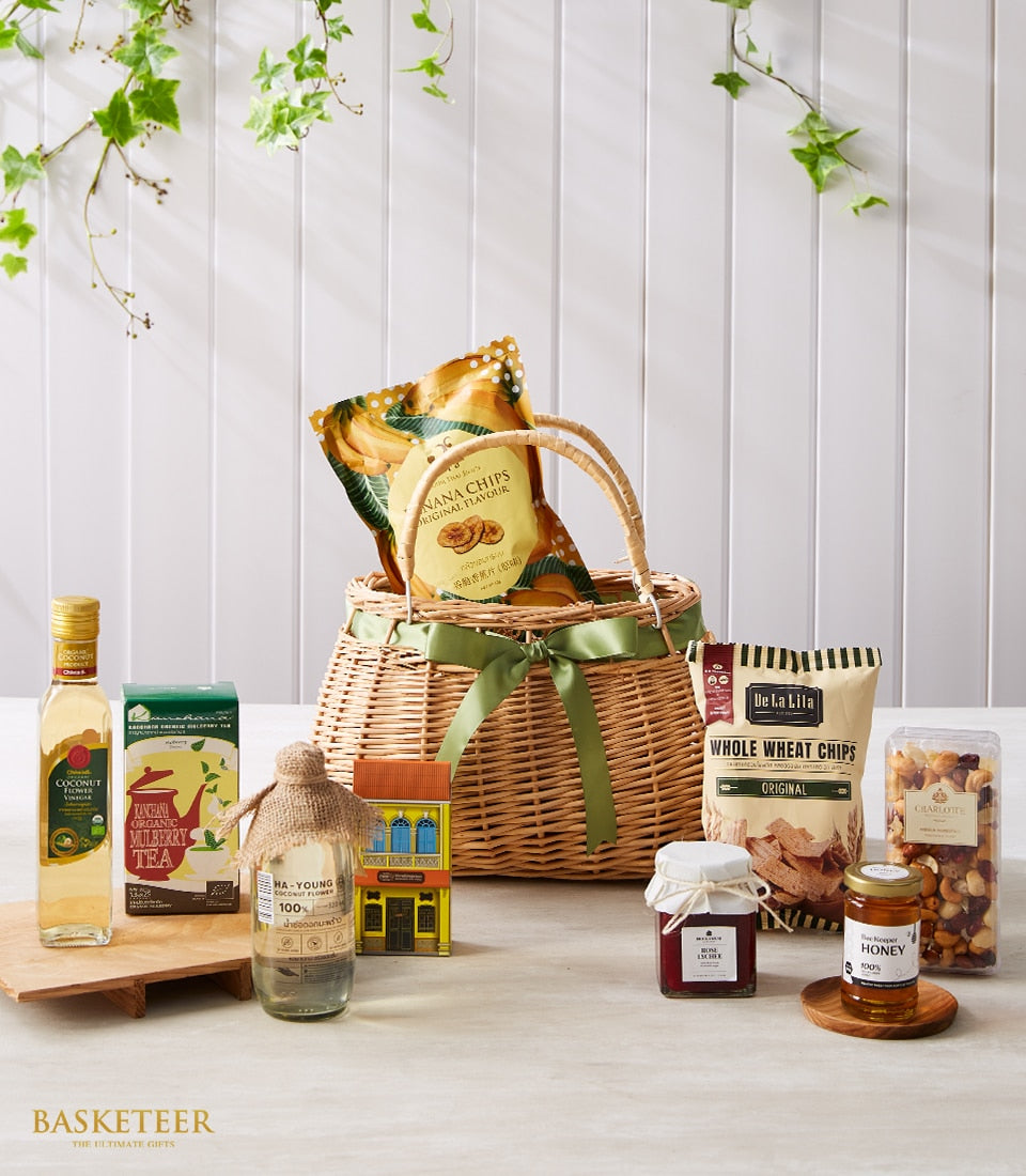 Woven gift basket with green ribbon filled with Thai gourmet treats including coconut flower vinegar, mulberry tea, honey,