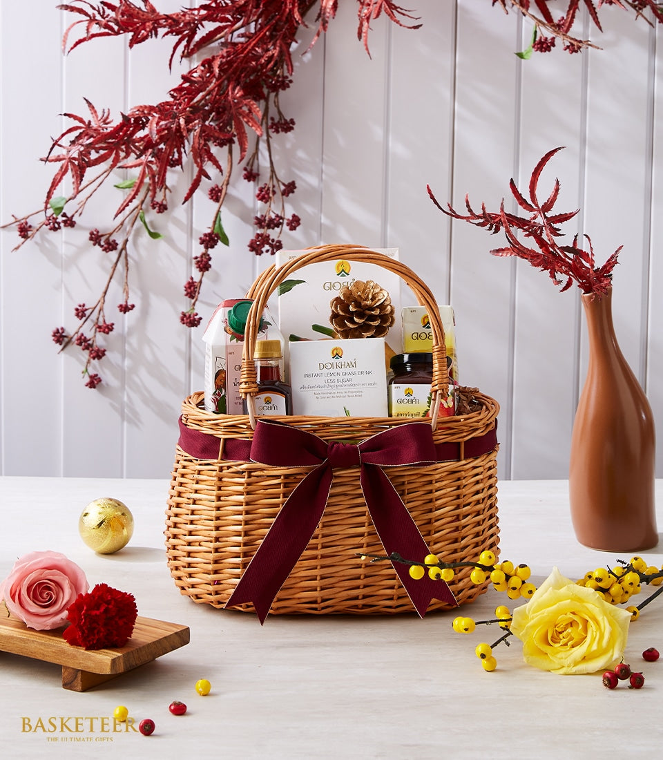 Elegant wicker gift basket with dark red bow, filled with Doi Kham premium gourmet items and natural florals