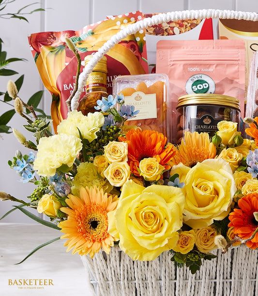Luxe gift basket with fresh yellow roses, gerbera daisies, gourmet coffee, artisan snacks, and organic treats