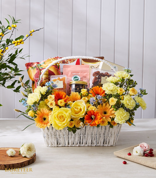 Luxury gift basket with fresh yellow roses, gerbera daisies, and gourmet treats in white woven basket