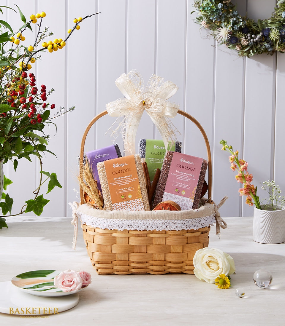 Woven basket gift set with premium Thai rice varieties, dried botanicals, and fresh flower arrangement in red, pink, and