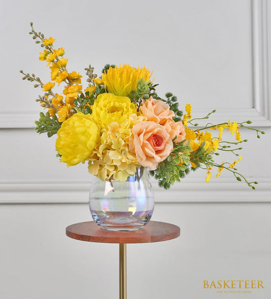 Yellow peony and hydrangea artificial flower arrangement in iridescent glass vase on gold stand