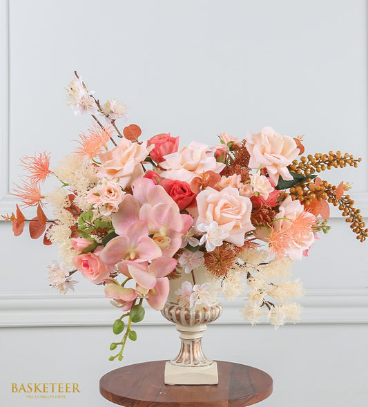 Peach and coral artificial flower arrangement in cream pedestal vase with gold accents, featuring roses and orchids