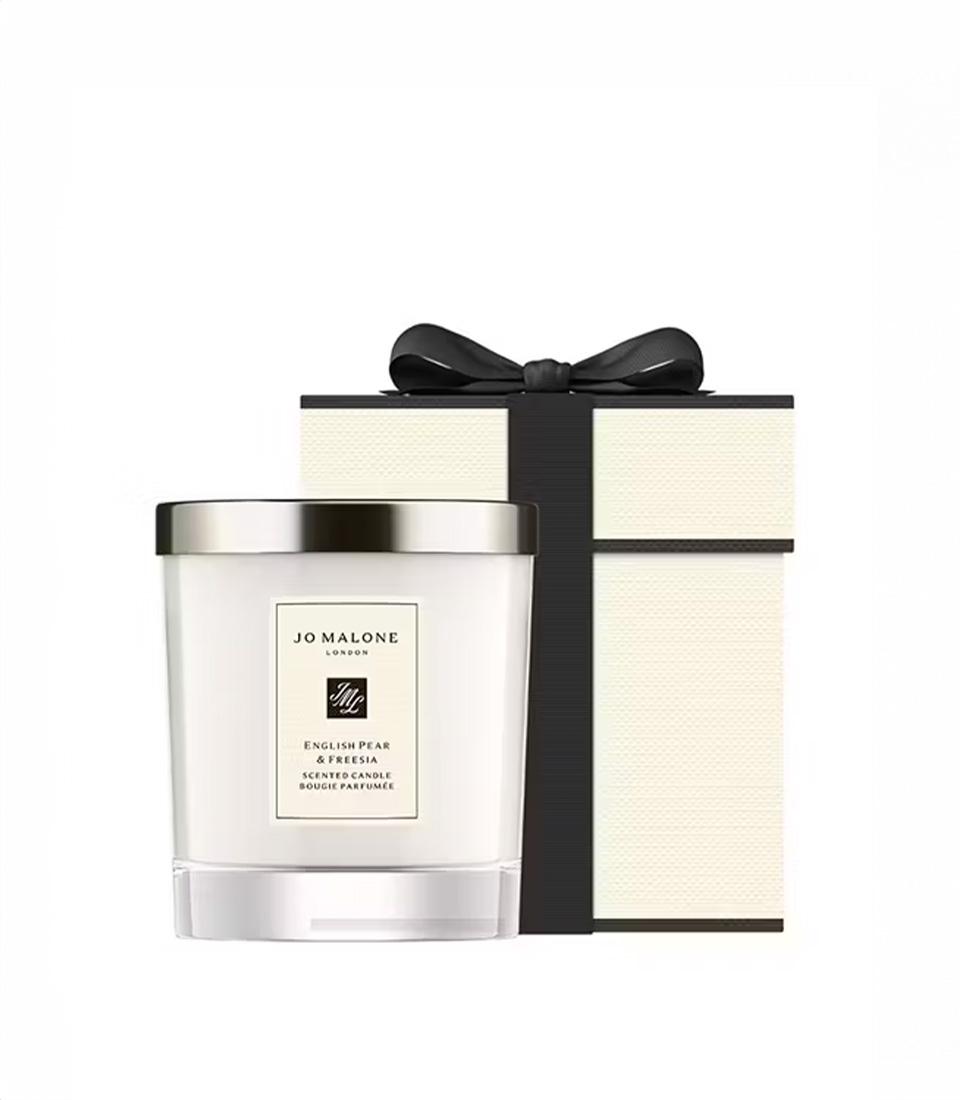 Basketeer luxury gift: Jo Malone London English Pear & Freesia candle, nestled near its signature cream and black gift box with ribbon. Premium hamper addition.