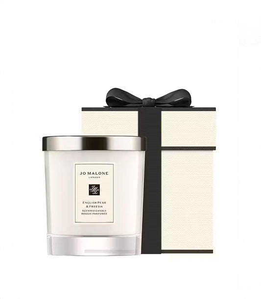 Basketeer luxury gift: Jo Malone London English Pear & Freesia candle, nestled near its signature cream and black gift box with ribbon. Premium hamper addition.
