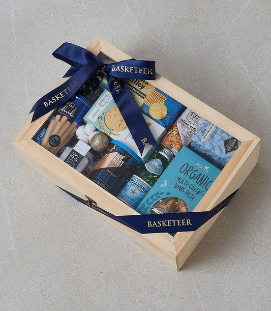 Wooden luxury gift box filled with gourmet crackers, cookies, coffee, and sparkling water, tied with navy ribbon