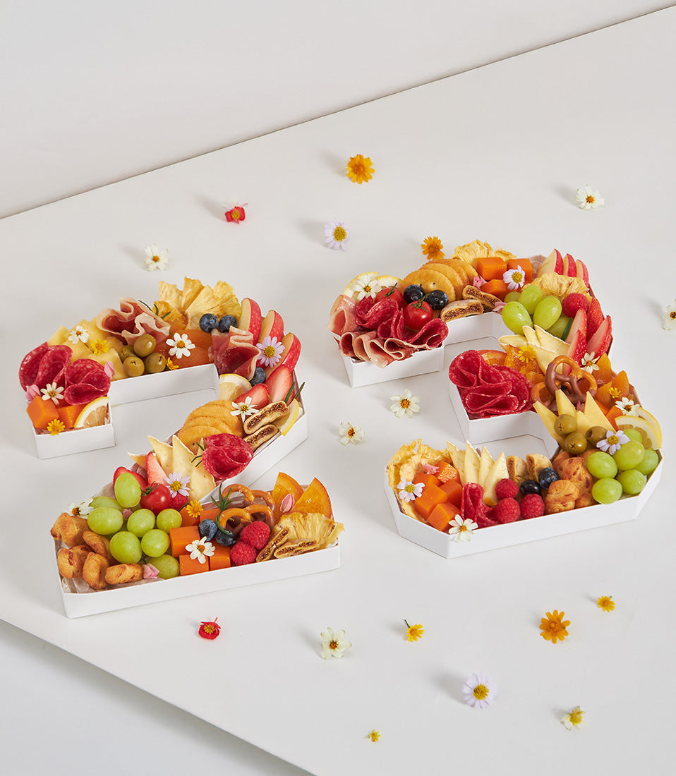 White number-shaped charcuterie board with artisan cheeses, cured meats, fresh berries, and edible flowers for milestone