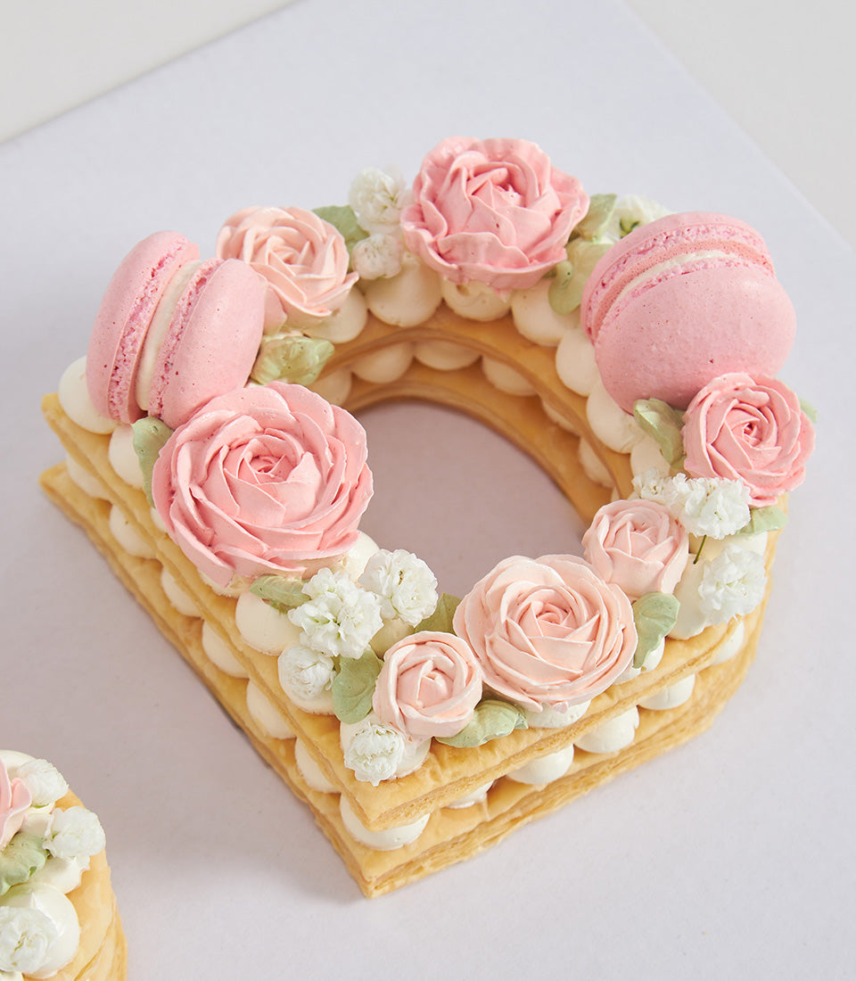 Birthday letter D cake with pink buttercream roses, white flowers, and macarons