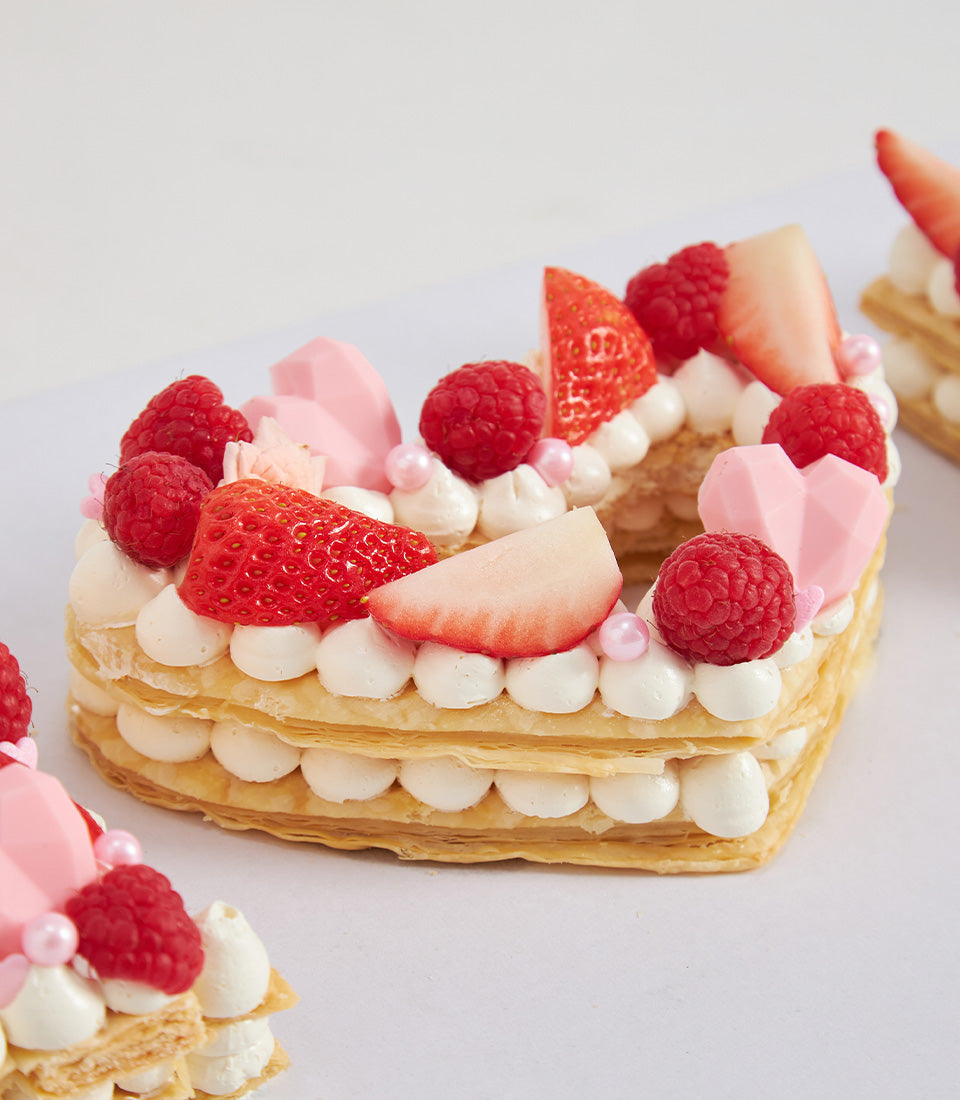 Heart-shaped mille-feuille cake with cream, fresh raspberries, strawberries, and pink chocolate hearts
