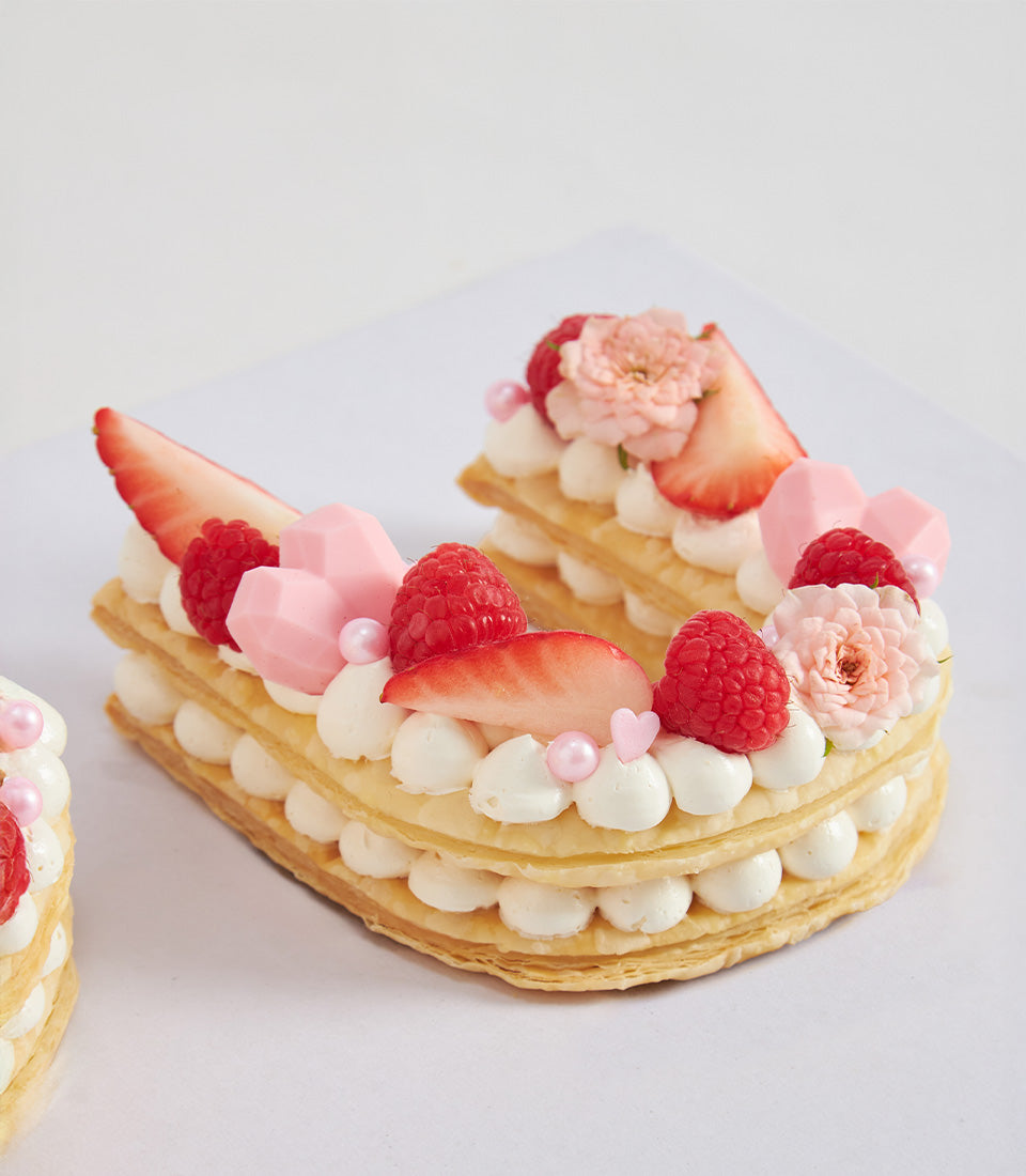 Letter U cake with raspberry, strawberry, cream, and pink hearts for birthday celebrations
