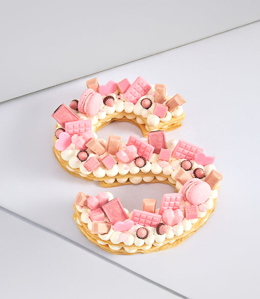 Pink puff letter S cake with cream filling, chocolate hearts, macarons and pink truffles for birthday celebrations