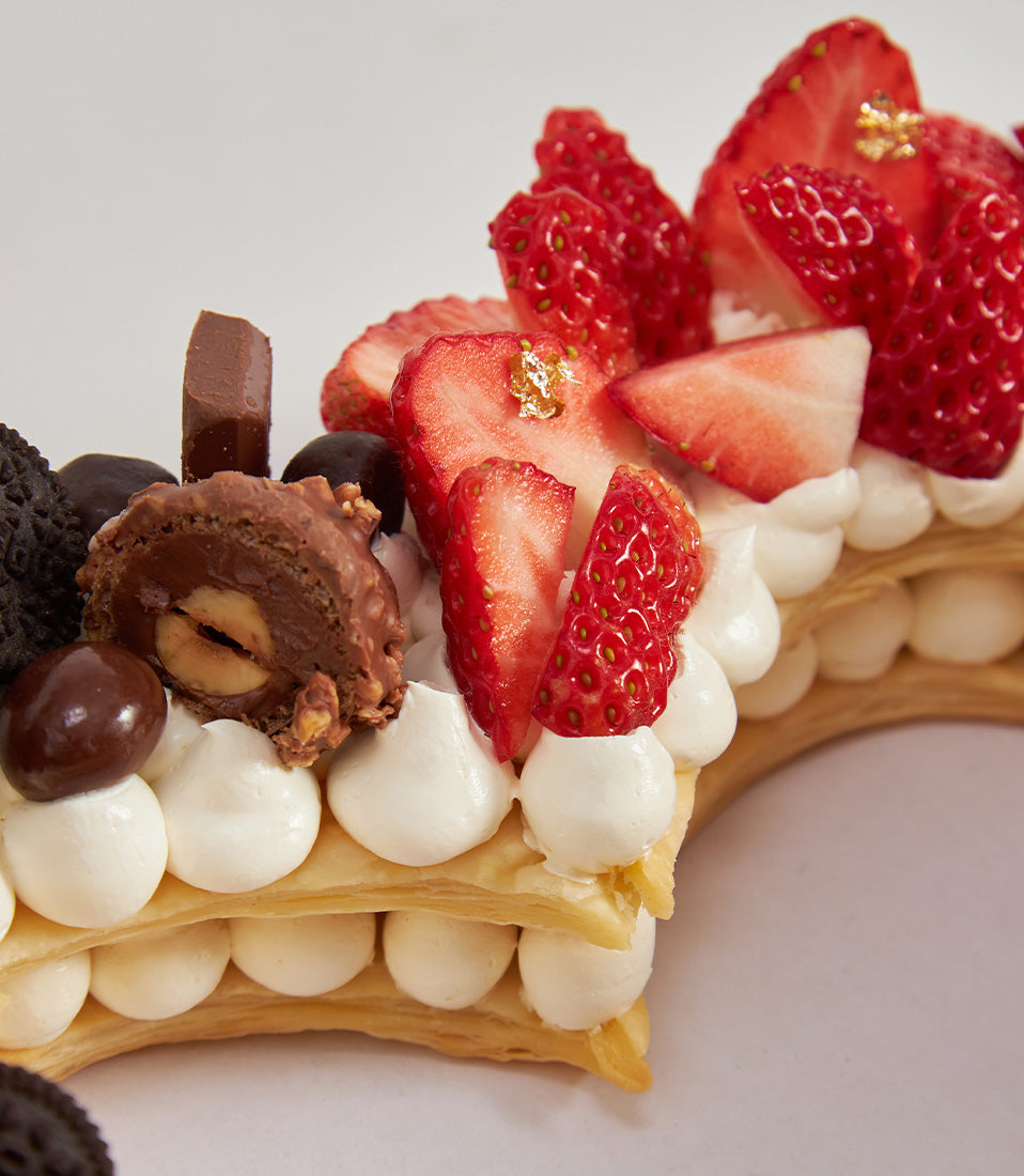 Heart-shaped chocolate and strawberry cream cake with golden pastry, chocolate pieces, and fresh berries