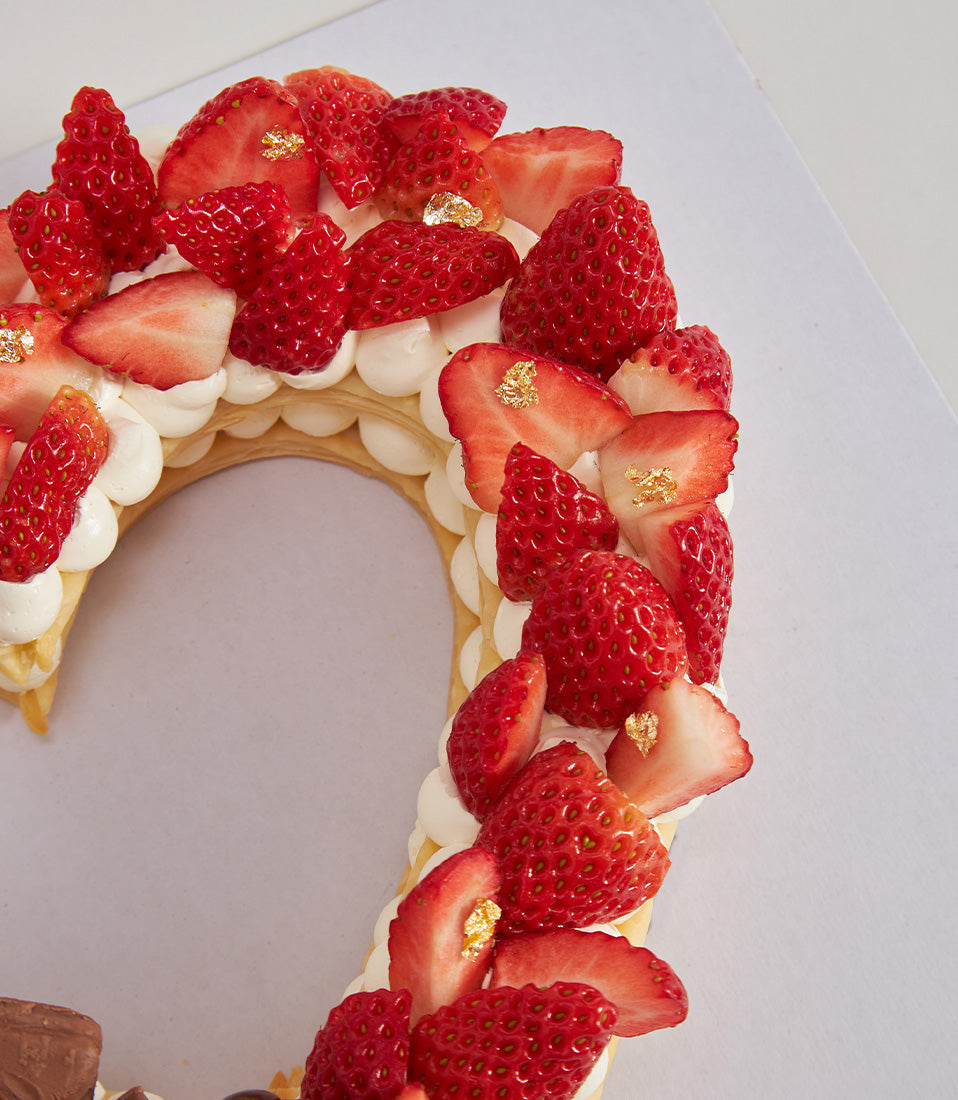 Heart-shaped chocolate and strawberry cake with gold-leaf strawberries and cream, perfect for birthdays