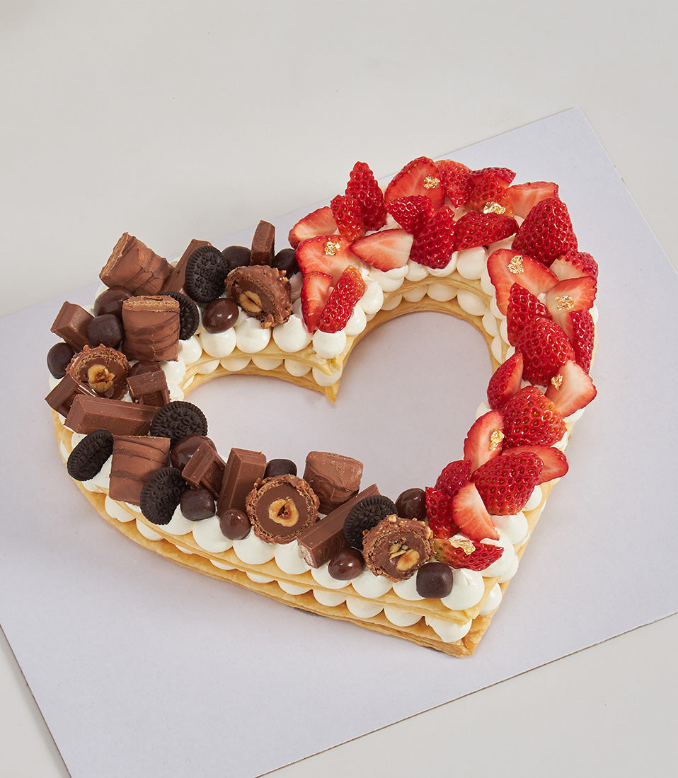 Heart-shaped cream tart split with fresh strawberries and chocolate assortment, artisan celebration cake
