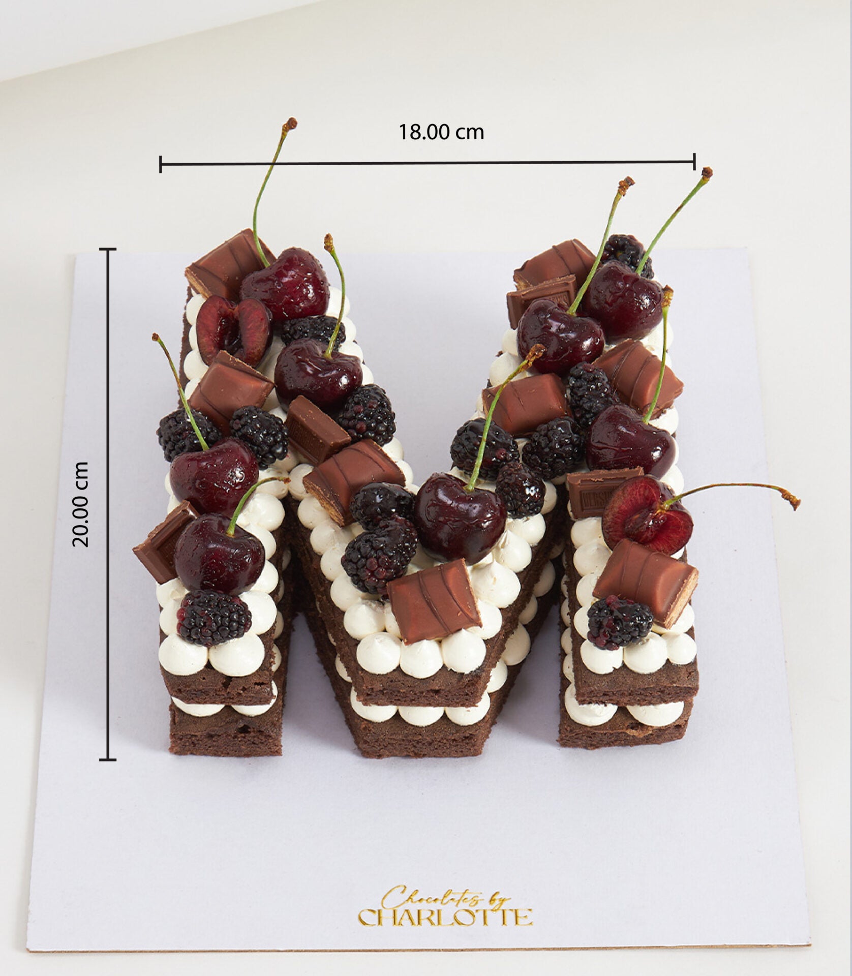 Chocolate cherry letter M cake with dark chocolate layers, white frosting swirls, fresh cherries and blackberries, perfect