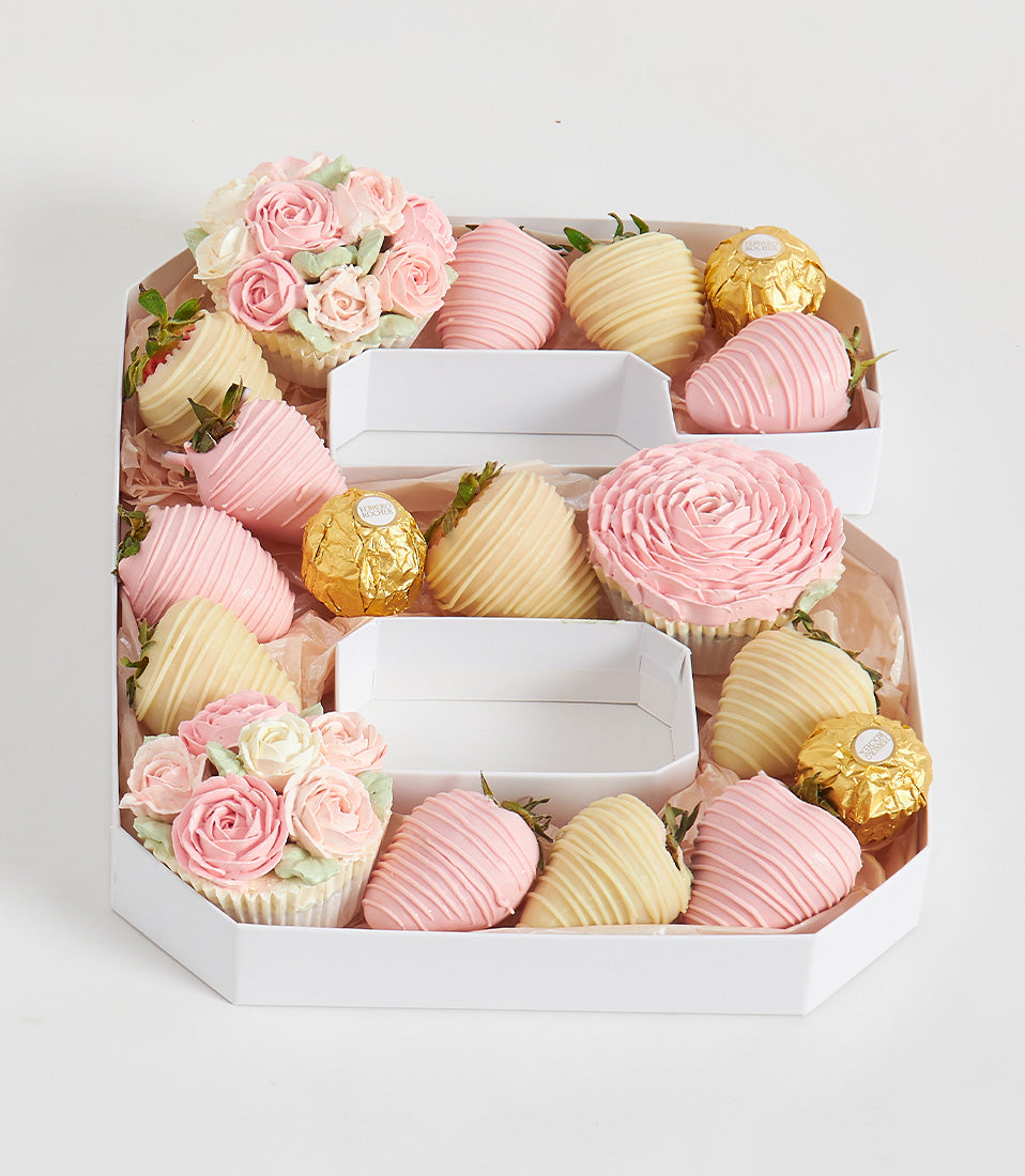 Hexagonal white gift box with number 6 arrangement of chocolate-covered strawberries, rose-decorated cupcakes, and Ferrero
