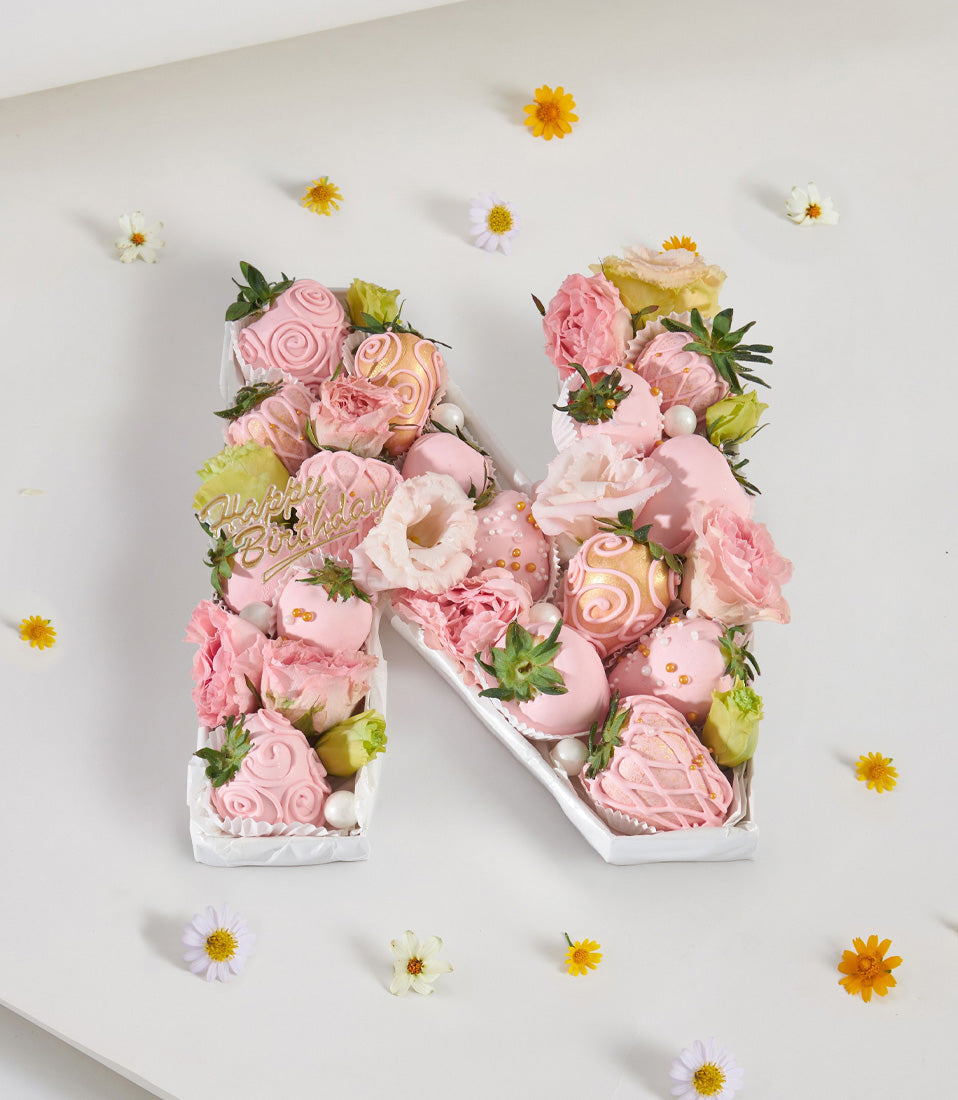 Pink letter cake "N" with chocolate-covered strawberries, fresh roses, and eustoma flowers for birthday celebrations