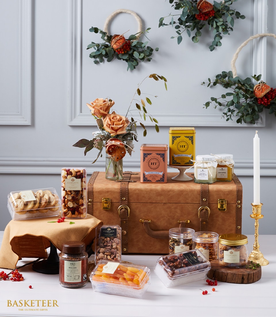 Luxury gourmet gift hamper with premium nuts, dried fruit, tea tins, coffee, candles, and peach roses in faux-leather trunk