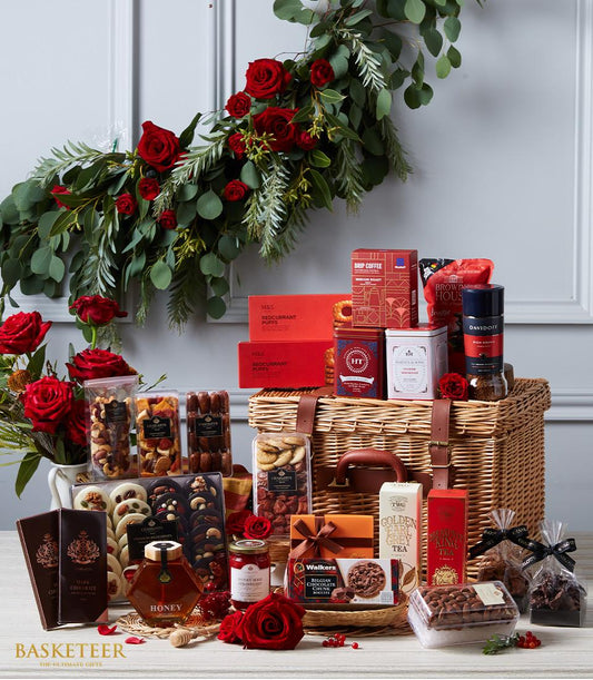 Luxury wicker gift hamper overflowing with gourmet tea, coffee, honey, nuts, and chocolates, surrounded by red roses