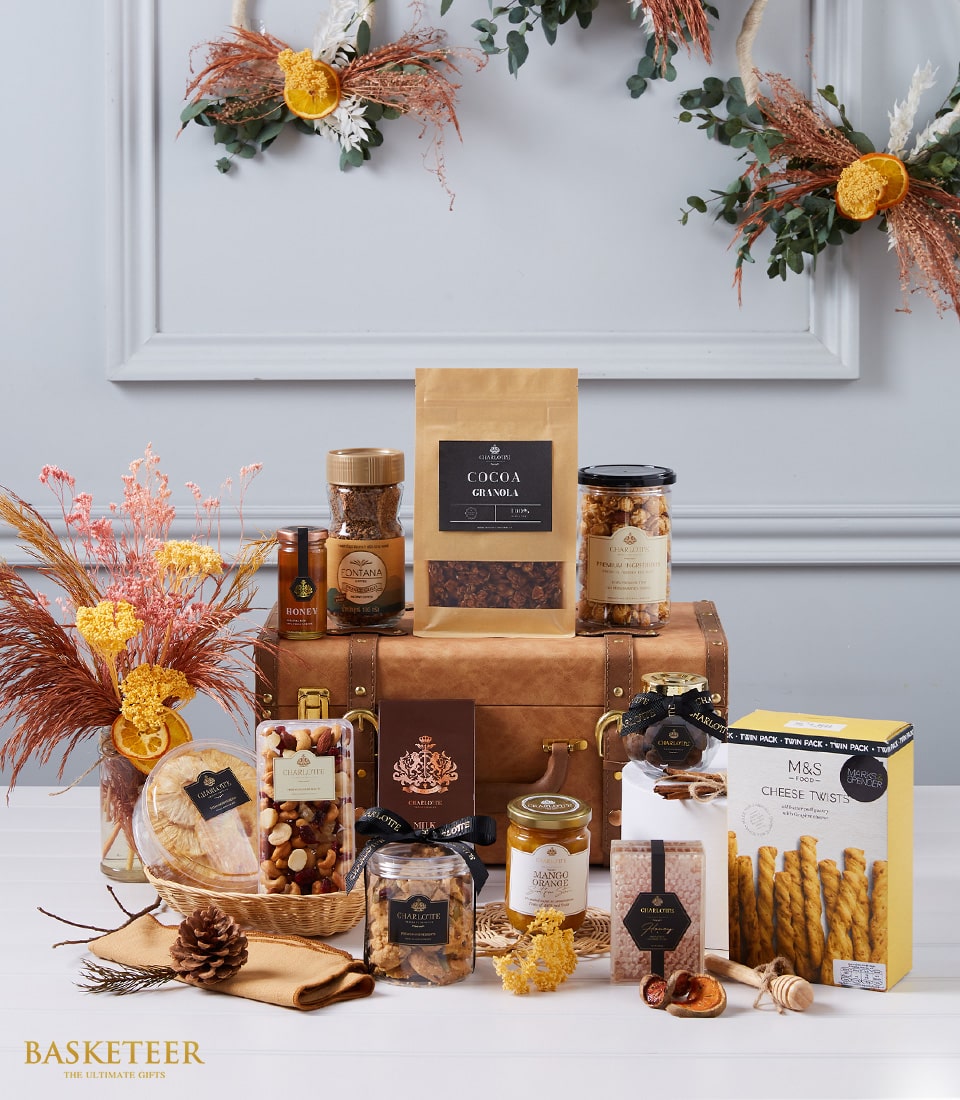 Luxury gourmet hamper with cocoa granola, honey, nuts, jam, and artisan treats in gold-labeled packaging, styled with dried
