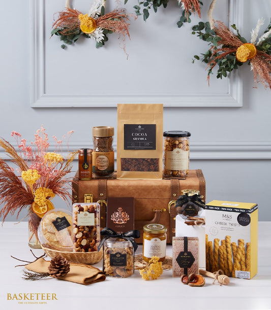 Luxury gourmet hamper with cocoa granola, honey, nuts, jam, and artisan treats in gold-labeled packaging, styled with dried