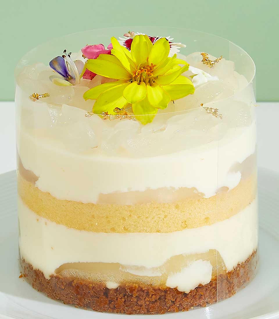 Mini layered cake with tropical fruit, cream, and edible flowers in clear cylinder