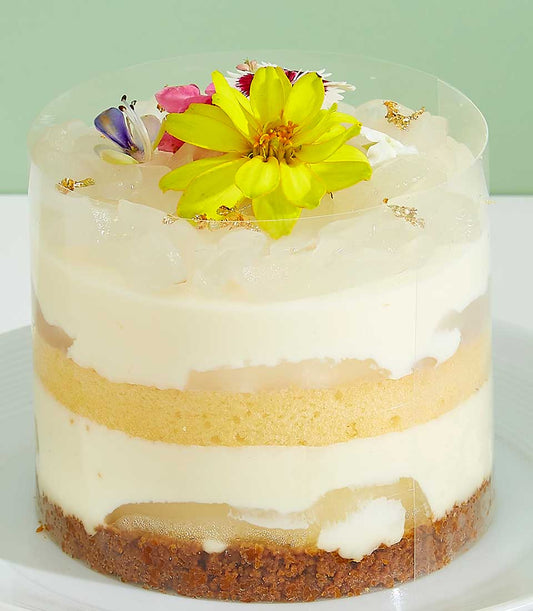 Mini layered cake with tropical fruit, cream, and edible flowers in clear cylinder
