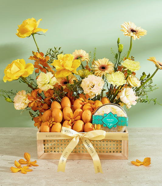 Wooden gift basket overflowing with Thai mangoes, yellow roses, and orange orchids tied with golden ribbon