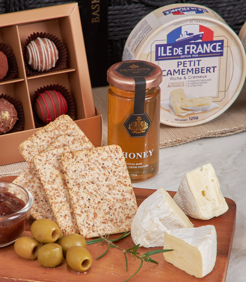 Gourmet cheese and chutney gift basket with crackers, honey, chocolates, and fresh rosemary garnish