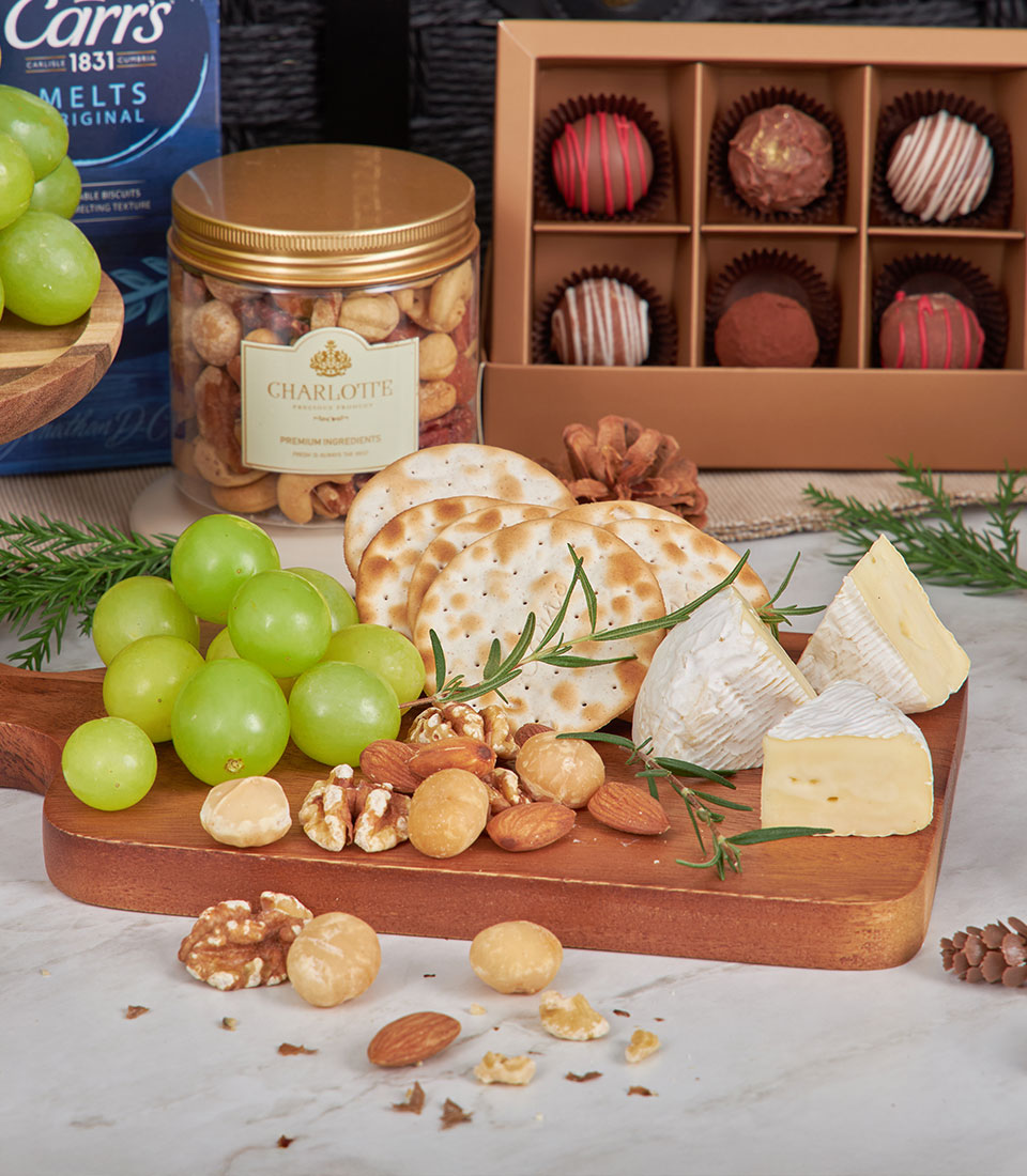 Gourmet gift basket with brie cheese, crackers, nuts, chocolates, and artisan ingredients on marble surface