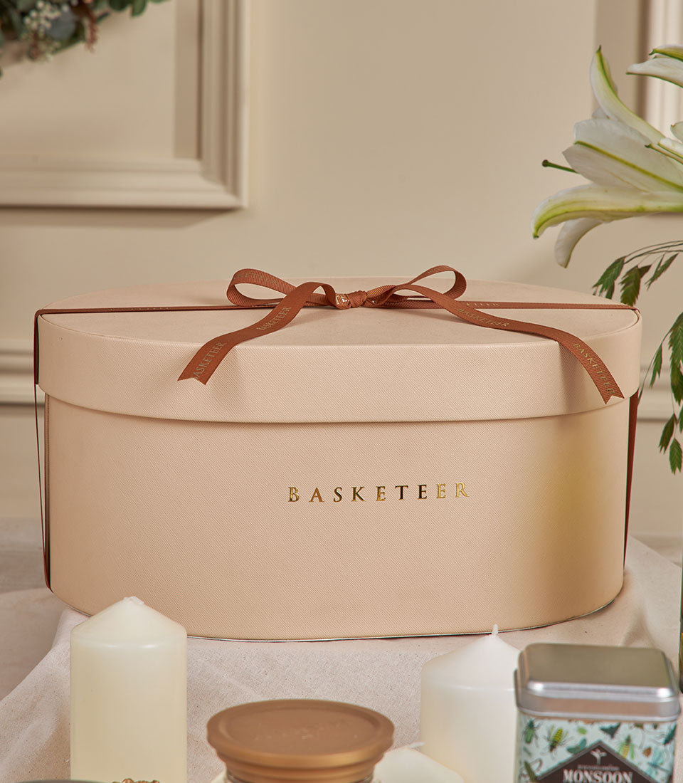 Beige oval gourmet gift basket with brown Basketeer ribbon, white candles, and lily for New Year gifting