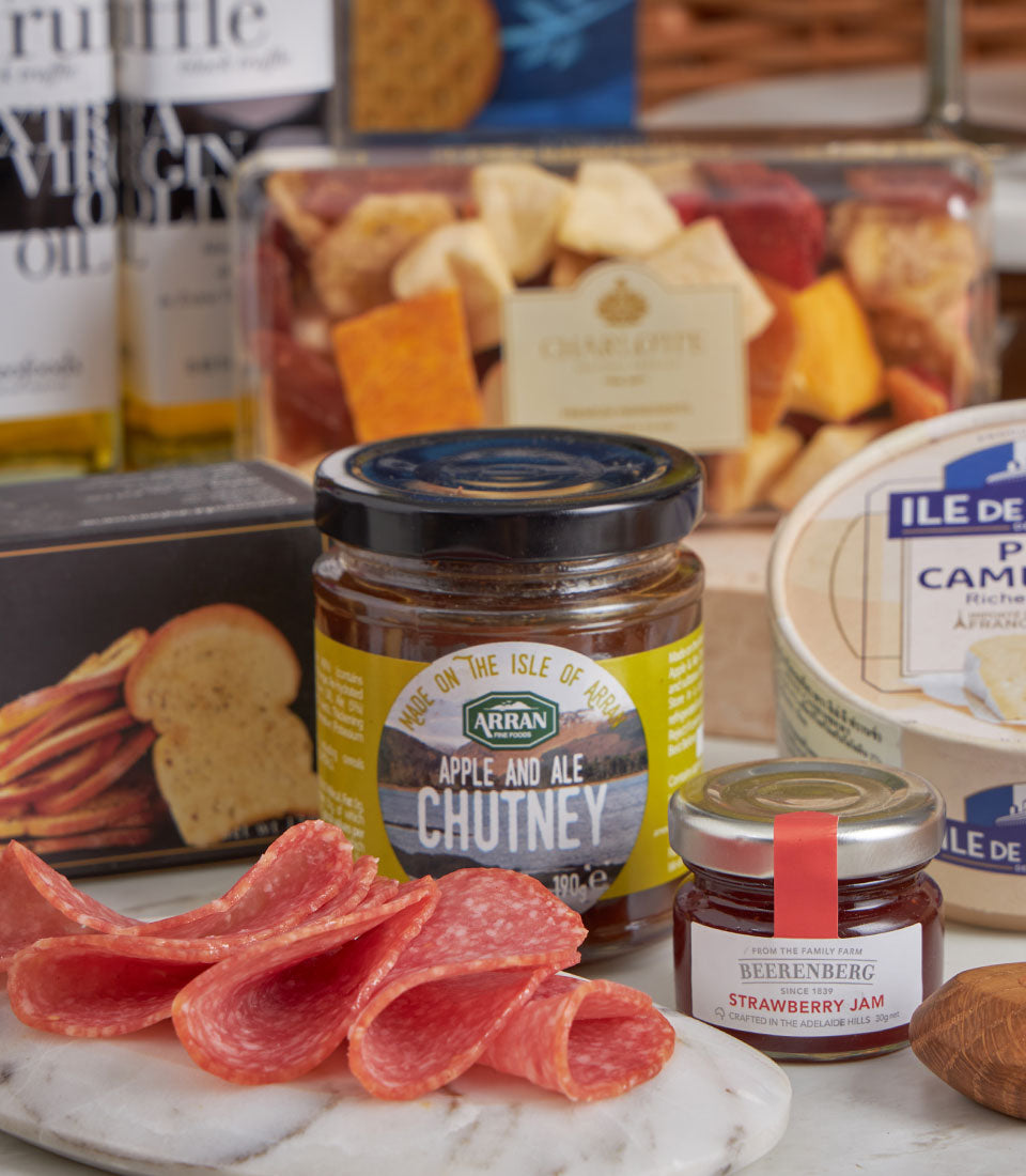 Luxury gourmet hamper with salami, artisan cheeses, chutneys, crackers, and premium olive oil on marble board