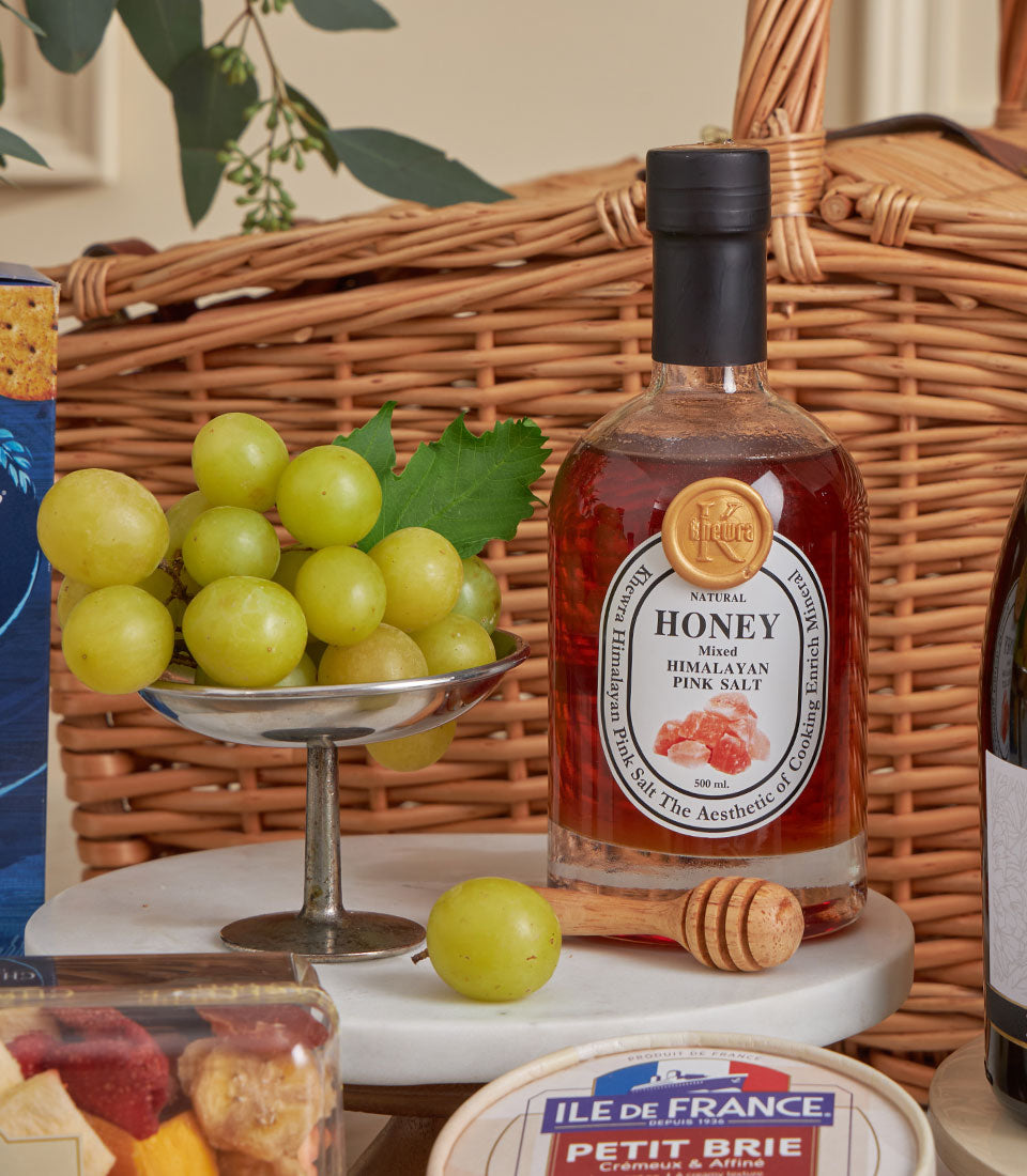 Gourmet hamper with Himalayan pink salt honey, artisan Brie cheese, green grapes, and dried fruit in wicker basket