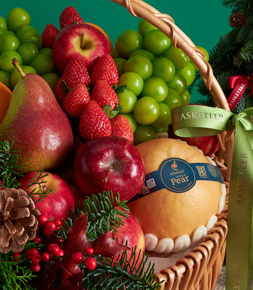 Woven Christmas fruit basket with red apples, strawberries, pears, green grapes, and festive pine greenery