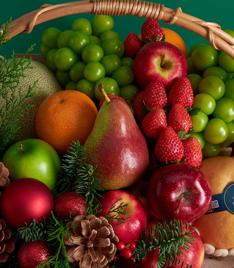 Luxury Christmas fruit basket with green grapes, red apples, strawberries, and melon, decorated with pine sprigs and