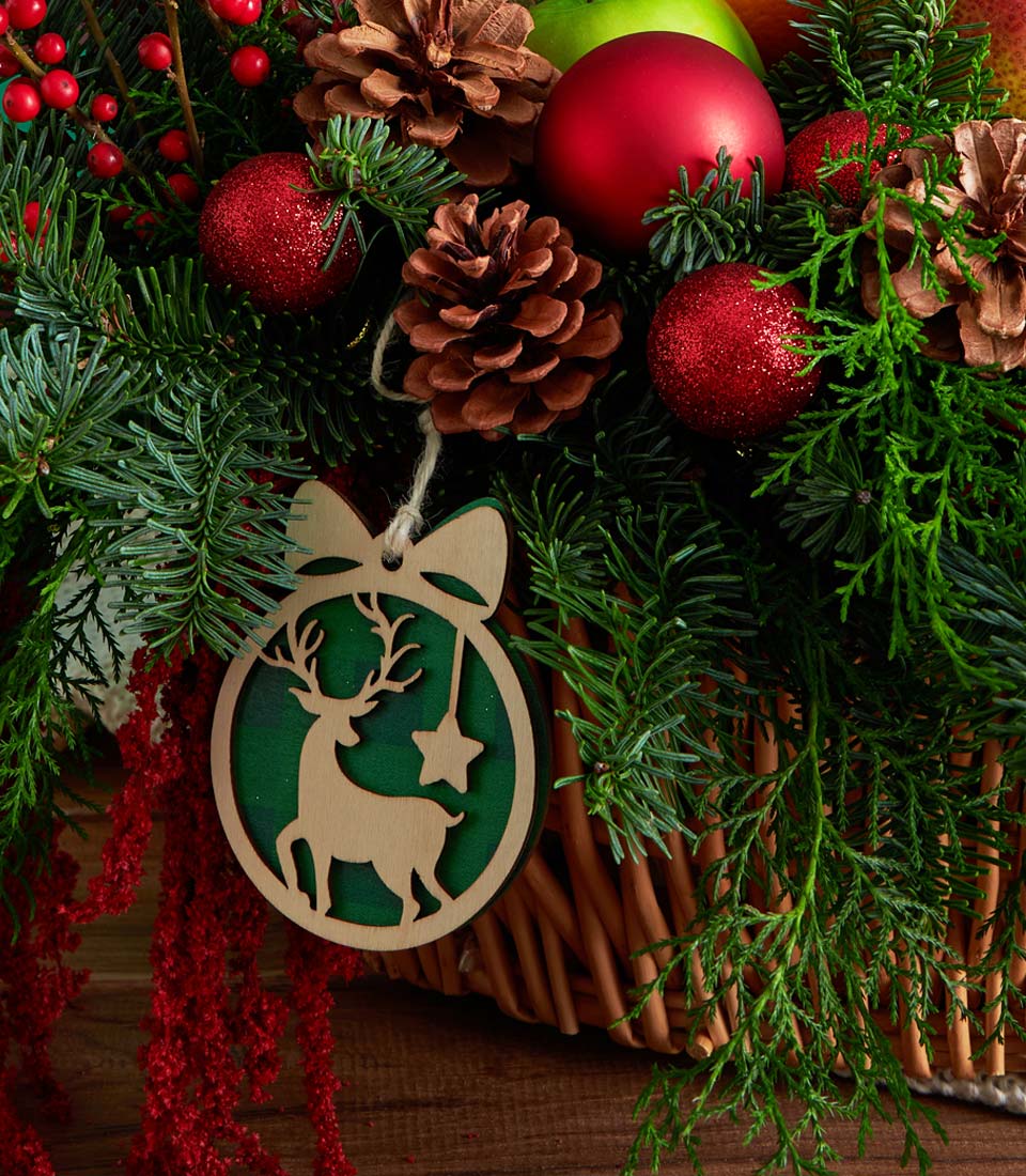 Festive wicker basket with pine branches, red ornaments, apples, pinecones and holiday foliage