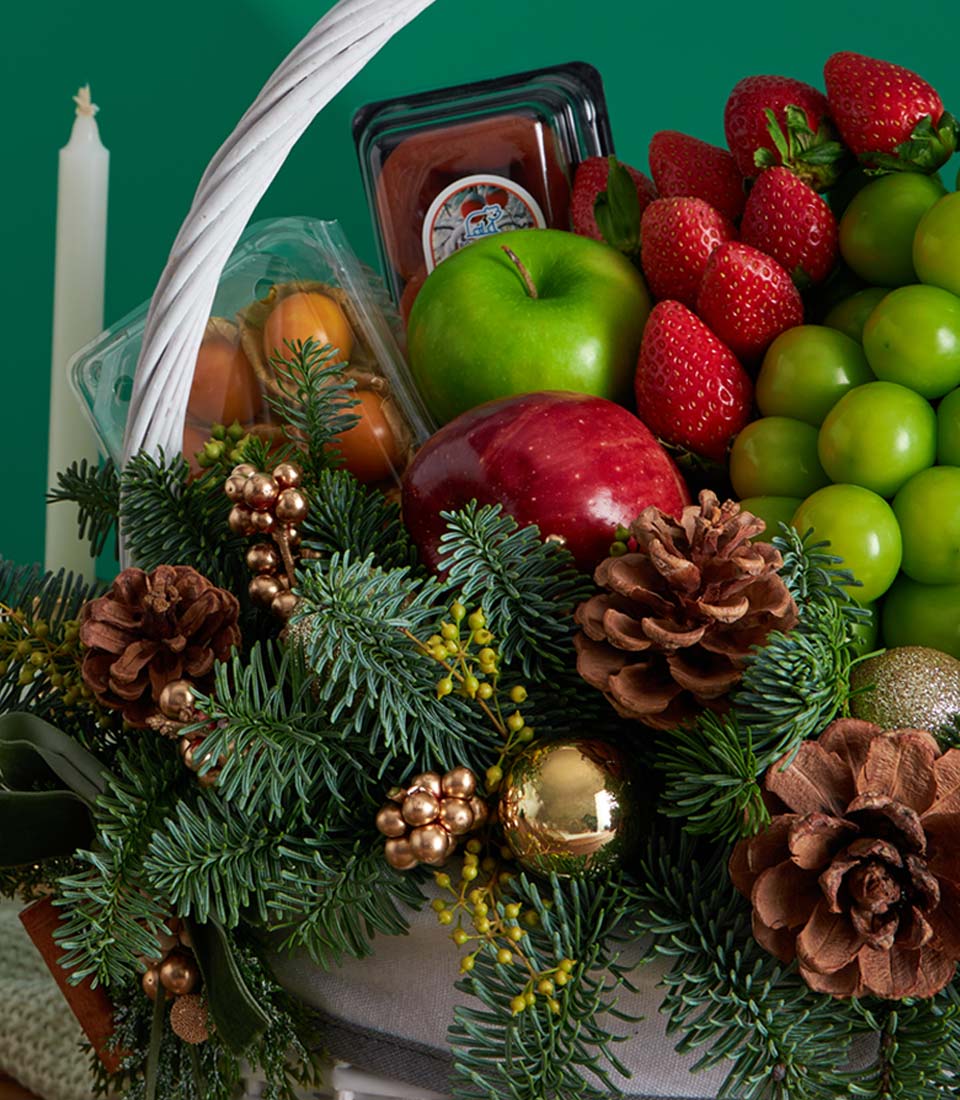 White Christmas fruit basket with fresh strawberries, apples, plums, pine branches, and gold ornaments