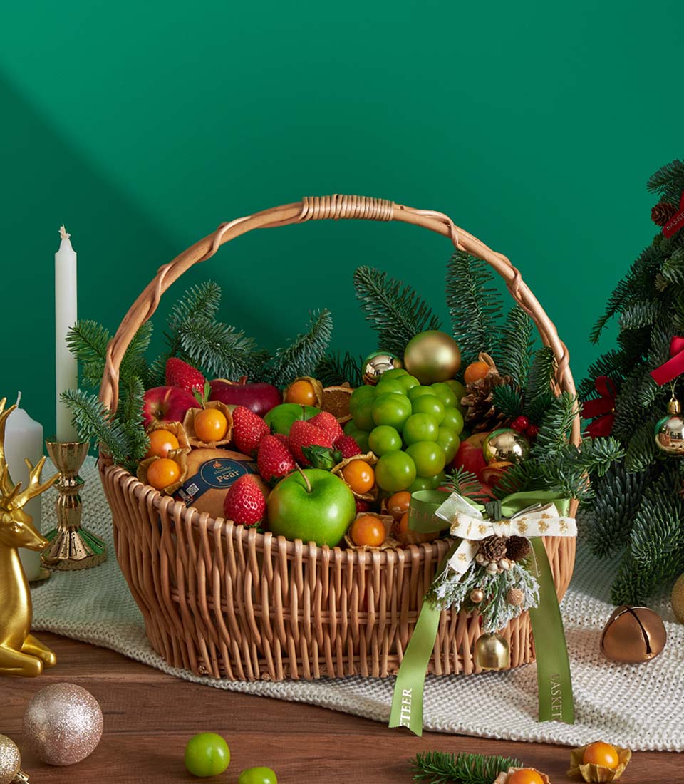 Festive red wicker fruit basket with fresh grapes, strawberries, apples, and physalis, adorned with evergreen, pinecones,
