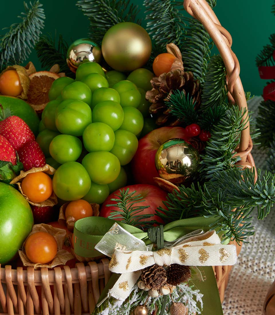 Festive red and green wicker Christmas fruit basket with grapes, apples, strawberries, and holiday ornaments