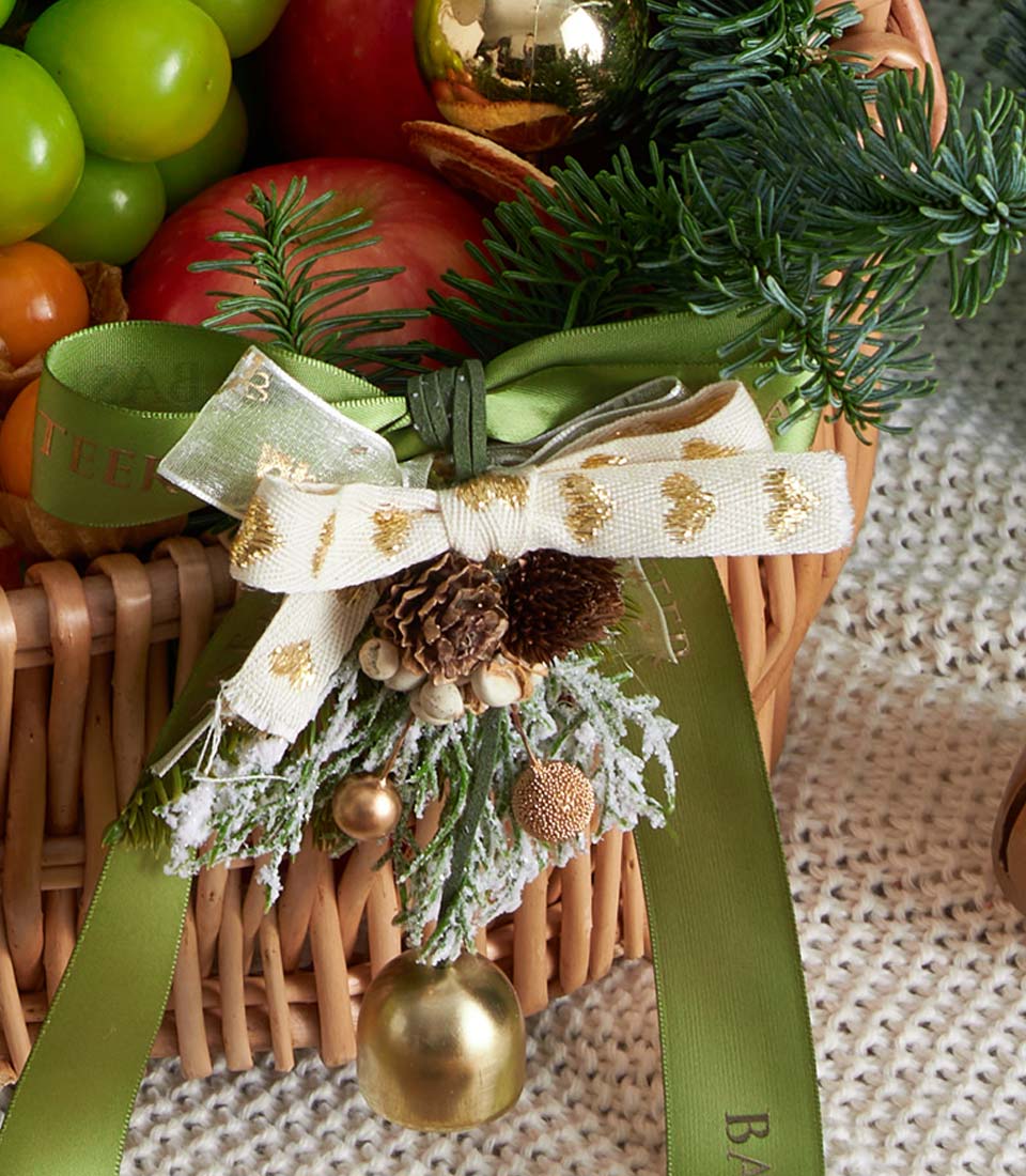 Festive red wicker fruit basket with fresh grapes, apples, and holiday greenery bow for Christmas gifting