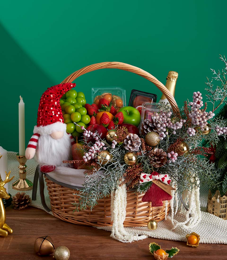 Festive Christmas fruit basket with fresh grapes, strawberries, apples, gnome decoration, and golden baubles