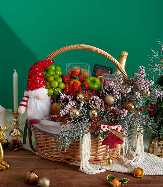 Festive Christmas fruit basket with fresh grapes, strawberries, apples, gnome decoration, and golden baubles