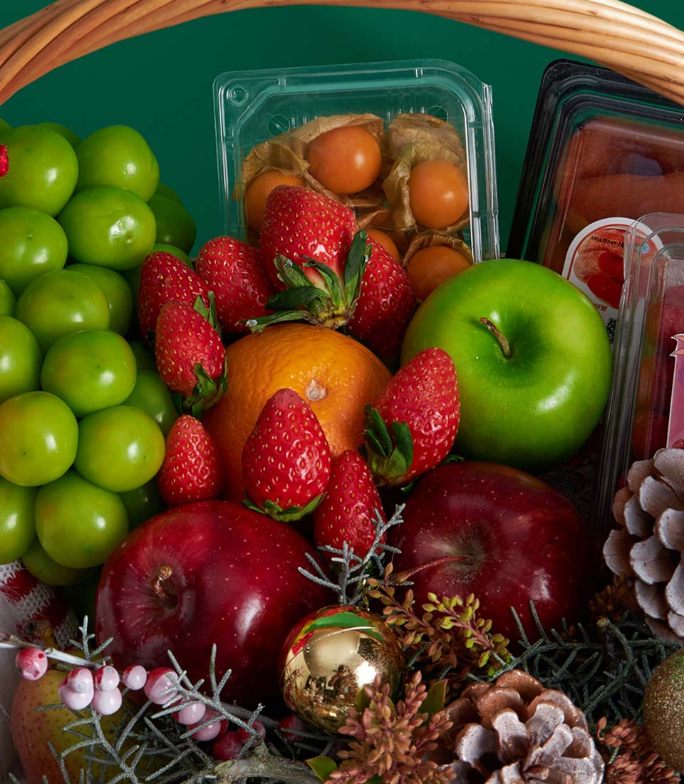 Premium Christmas fruit basket with fresh strawberries, apples, grapes, and physalis with festive gold ornament and Santa