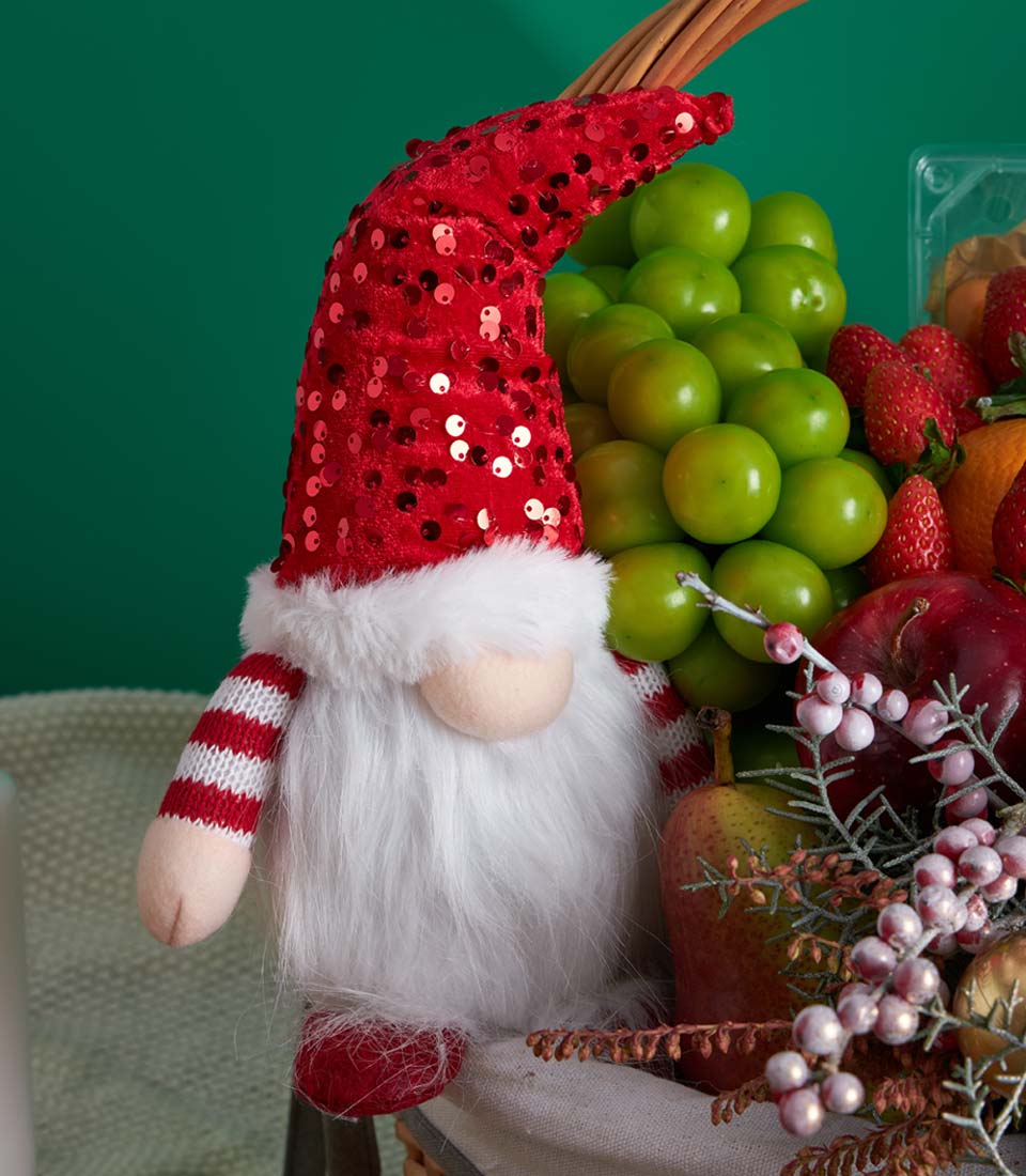 Festive Christmas fruit basket with red sequined gnome, fresh grapes, strawberries, and mixed fruits in woven basket